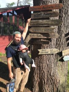 Me and Nina visiting Isabella Freedman Jewish Retreat in Connecticut, with my hand on a signpost pointing to Reb Zalman’s home and gesturing at the signpost pointing to Urban Adamah.