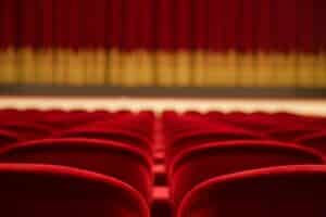 Photo of red theater chairs looking at a stage with a red curtain